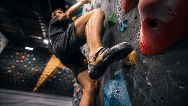 Wspinacz opiera stopę na stopniu i pracuje biodrem na boulderze